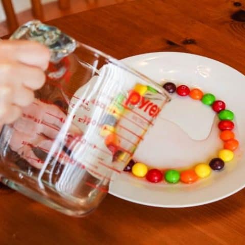 Girl pouring water on plate with Skittles