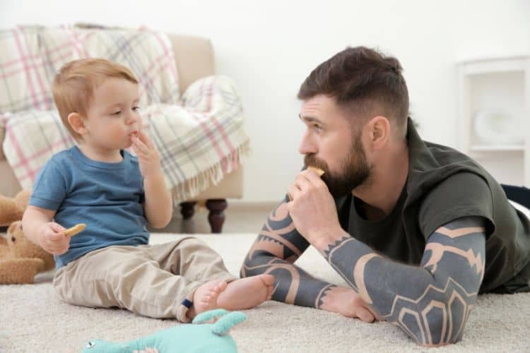 Dad and toddler looking at each other sitting on floor eating food