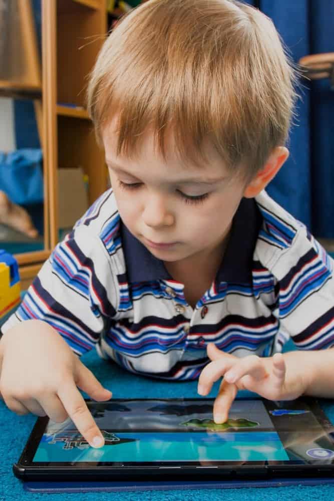 Boy lying on stomach playing on his tablet