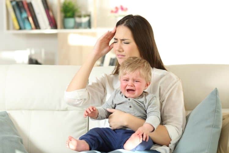 Exhausted mom holding a crying toddler while sitting on the couch