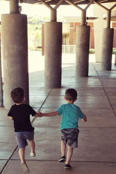 Two toddlers running away from the camera holding hands
