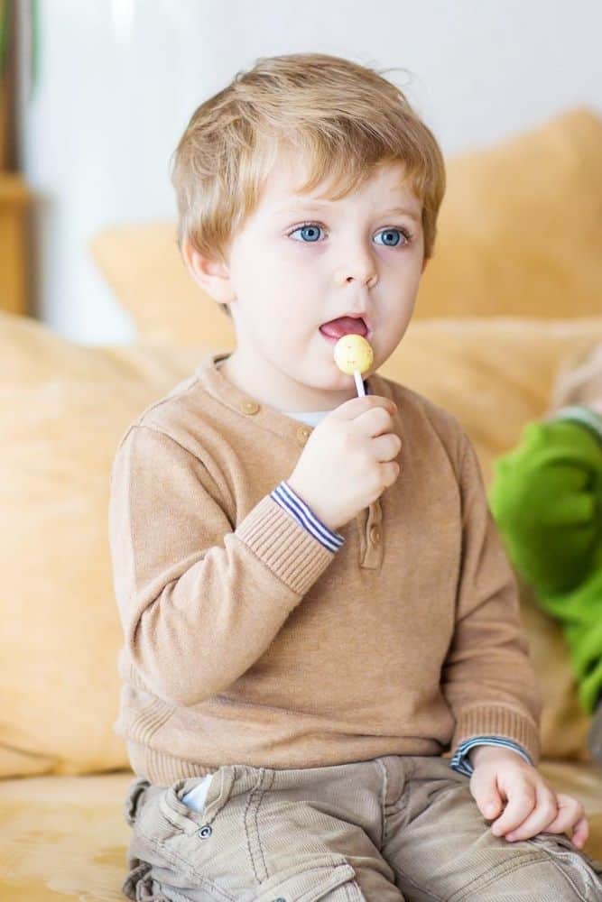 Toddler holding a sucker while sitting on a couch watching something off camera